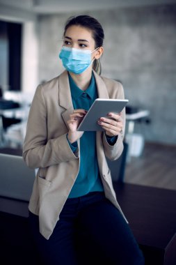 Female entrepreneur with face mask working on digital tablet in the office.