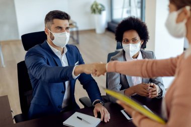 Human resource team fist bumping with a candidate during a job interview. They are wearing protective face masks due to coronavirus pandemic. 