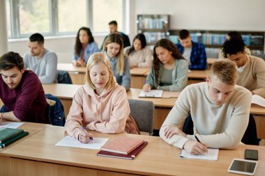 College student and her classmates writing an exam in the classroom.