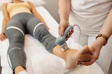 Fizyoterapist, rehabilitasyon merkezinde elektroterapi gören atletik bir kadının eklemlerini tedavi ediyor..