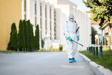 Disinfectant worker in protective suit sanitizing empty city streets during COVID-19 epidemic clipart