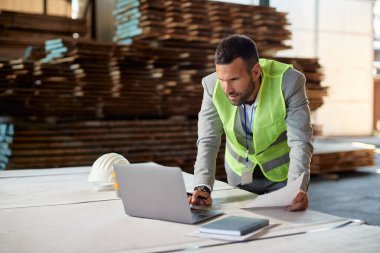 Mid adult businessman using laptop while working at warehouse distribution department.