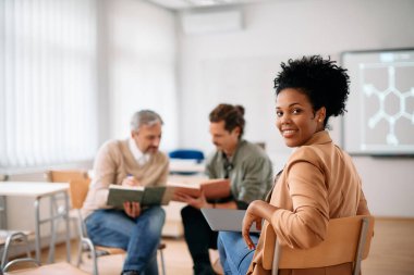 Portrait of happy African American professor during class at lecture hall. Her student are in the background.