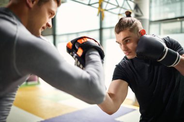Young athlete exercising boxing with his instructor during sports training at health club.