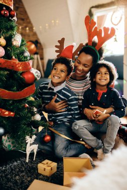 Mutlu siyah anne çocuklarını kucaklarken Noel ağacının yanında oturup tatilin tadını çıkarıyor.. 