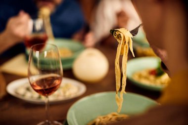 Close-up of woman eating pasta while dining with friends at home. 