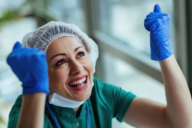 Young female doctor with hands raised feeling excited and looking up while working at medical clinic. 