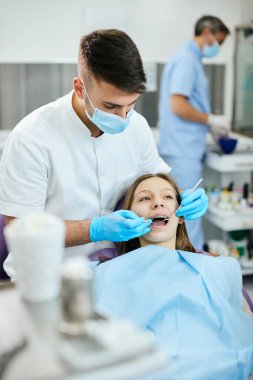 Young dentist examining teeth braces of teenage girl during dental procedure at dentist's office