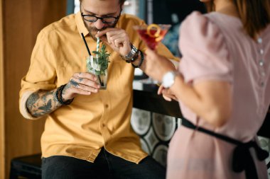 Young man drinking mojito cocktail during Valentine's date with his girlfriend in a bar. 