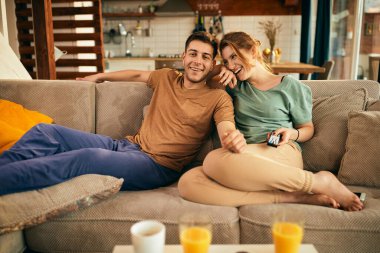 Happy couple having fun while watching movie and relaxing on the sofa in the living room. 