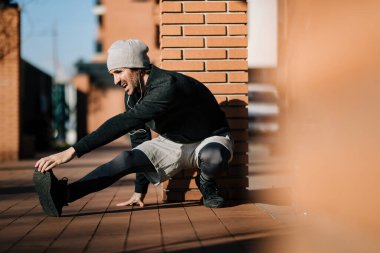 Young male athlete doing stretching exercises while having sports training outdoors. Copy space. 