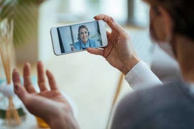 Close-up of woman using smart phone and having video call with healthcare worker during virus pandemic. 