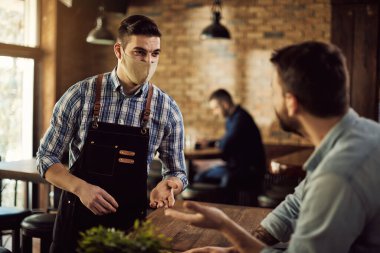 Waiter taking order from a guest while wearing face mask in a cafe due to coronavirus pandemic. 