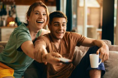 Happy woman and her boyfriend having fun while changing channels on TV in the living room. 