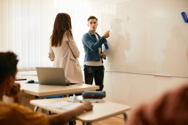 High school students writing mathematical formula on whiteboard and talking to his professor in the classroom. Copy space.