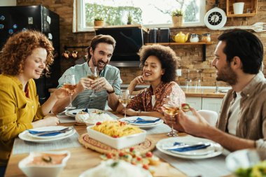 Young happy adults talking while drinking wine at dining table during lunch time. 