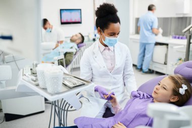 African American dentist holding little girl's hand and consoling her during dental procedure at dentist's office.