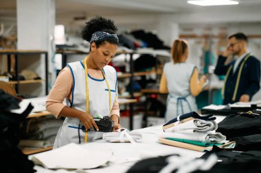 African American seamstress working at clothing design studio and labelling finished textile products.