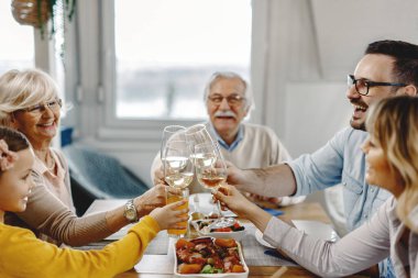 Happy multi-generation family having fun while toasting during a meal in dining room. 