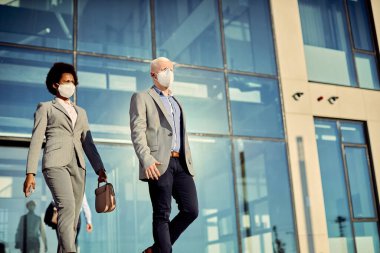 Low angle view of business people wearing protective face masks while walking outdoors. Focus is on businessman. Copy space. 
