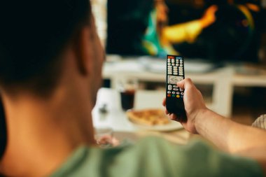 Close-up of man changing channels while watching TV at home. 
