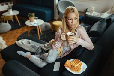 Young woman thinking while drinking coffee and relaxing in the living room. 