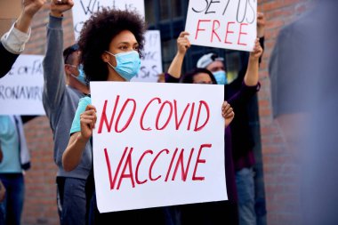 African American woman wearing protective face mask and holding 'No COVID vaccine' while participating in anti-vaccination demonstrations. 