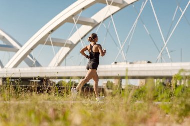Back view of athletic woman running while exercising outdoors. Copy space.