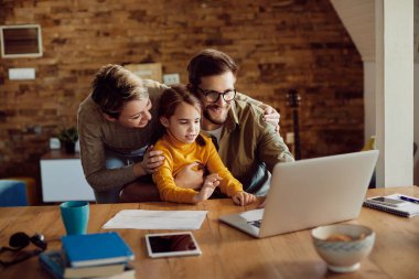 Happy parents and their daughter using computer at home.