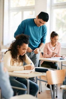 Smiling teacher helping African American teenage girl with a lecture in the classroom. 