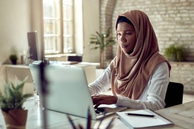 Muslim businesswoman using laptop while working at her office desk. 