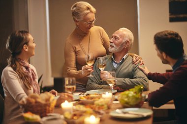 Happy senior couple celebrating anniversary and toasting with wine during family dinner at dining table. 