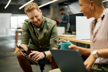 Happy creative business people cooperating while using digital tablet in the office. Focus is on man. 