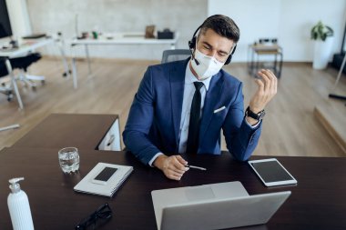 Happy entrepreneur using laptop while having video call in the office. He is wearing protective face mask due to coronavirus epidemic. 