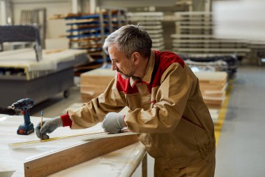Manual worker marking measurements on a piece of wood at carpentry workshop.