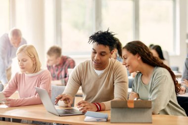 Happy black student and his female friend studying on laptop during a class at college classroom.