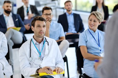 Large group of healthcare workers and business people attending educational event at conference hall. Focus is on male doctor. 