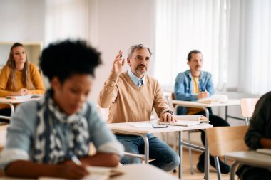 Mature man raising his arm while attending lecture at university classroom.