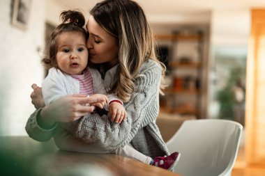 Young mother showing affection to her small daughter while kissing her at home. 