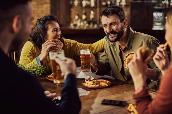 Happy man having fun with his friends while drinking beer and eating burgers in a pub.