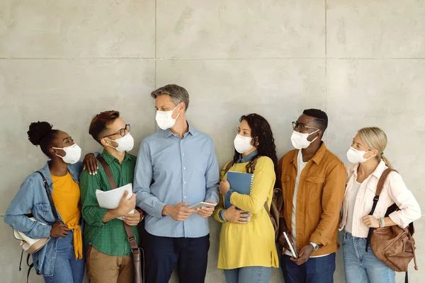 University professor and his students wearing protective face masks while standing by the wall and communicating. Copy space.