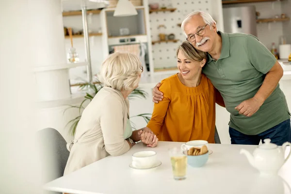 Happy senior couple talking with their adult daughter who came to visit them at home.