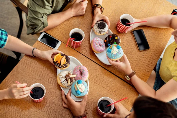 High angle view of unrecognizable people eating glazed doughnuts at the table in a cafe.