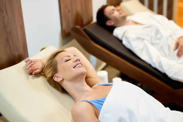 Smiling woman relaxing with eyes closed while relaxing with her husband at health spa.