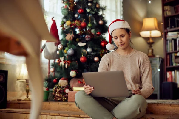 Woman Wearing Santa Hat Using Laptop While Sitting Christmas Tree — ストック写真