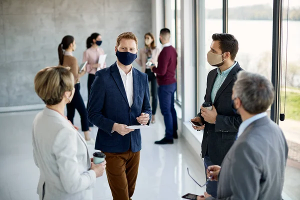 Group of colleagues standing in a lobby after business seminar and talking. They are wearing protective face masks due to COVID-19 pandemic.