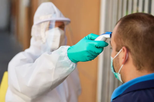 Close-up of healthcare worker in hazmat suit measuring man\'s temperature with infrared thermometer during coronavirus pandemic.