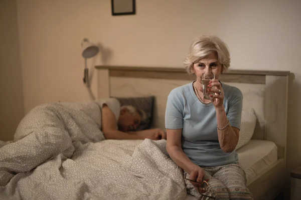 Yaşlı Kadın Kocası Uyurken Yatak Odasında Bir Bardak Içiyor — Stok fotoğraf