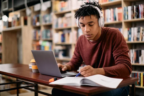 Young Black Student Reading While Using Laptop Studying Library — ストック写真