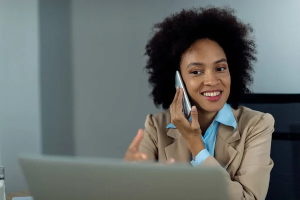 Happy African American Businesswoman Using Computer Talking Cell Phone While — ストック写真